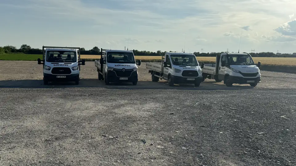 Štyri valníkové nákladné autá Konkret Line zoradené pred poľom